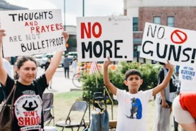 Kids protesting gun violence are holding signs that say "Thoughts and prayers are not bullet proof" and "No more. No guns!"