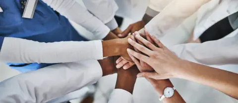 Hands of a diverse group of doctors come together to represent unity and strength of purpose in supporting gun violence legislation